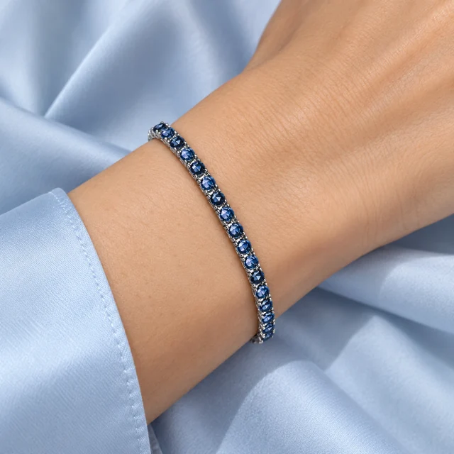 Coroné blue sapphire tennis bracelet worn on the wrist beside pale-blue silk