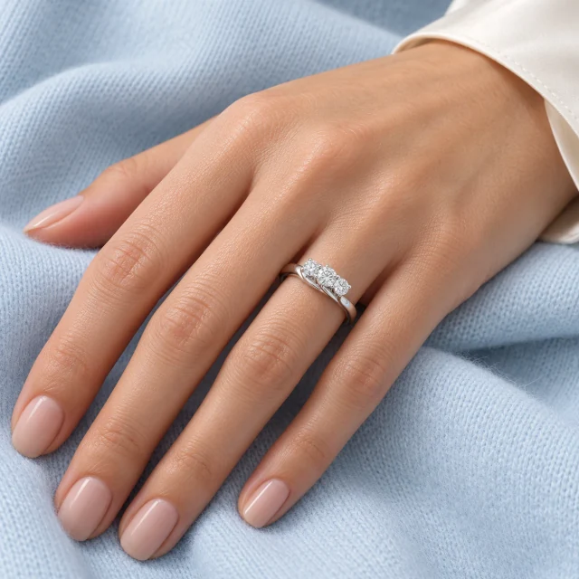 Flower Trilogy Ring worn on the ring finger against pale blue fabric